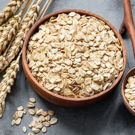 Oat flakes or rolled oats in wooden bowl on concrete table background. Healthy eating concept